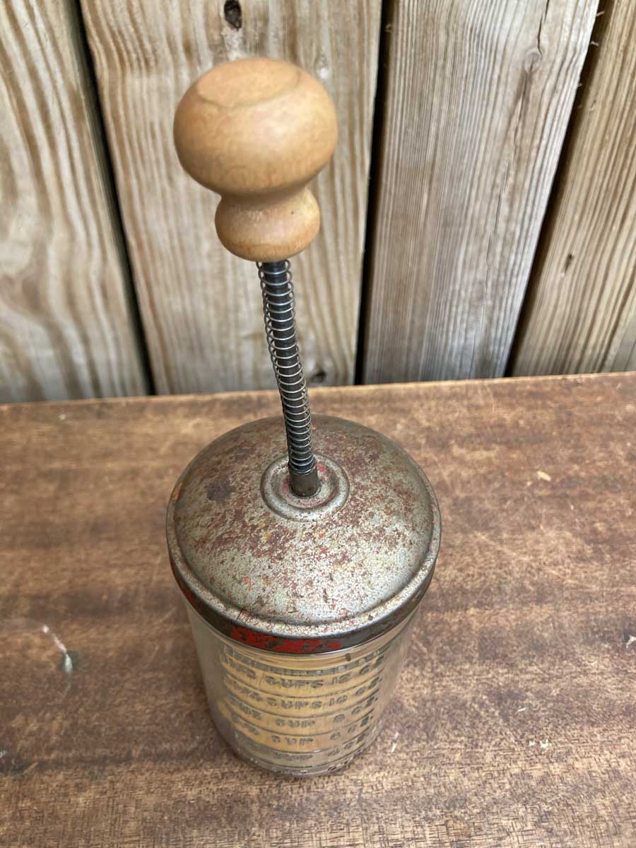 Antique nut chopper with a red handle with a glass jar on a solid