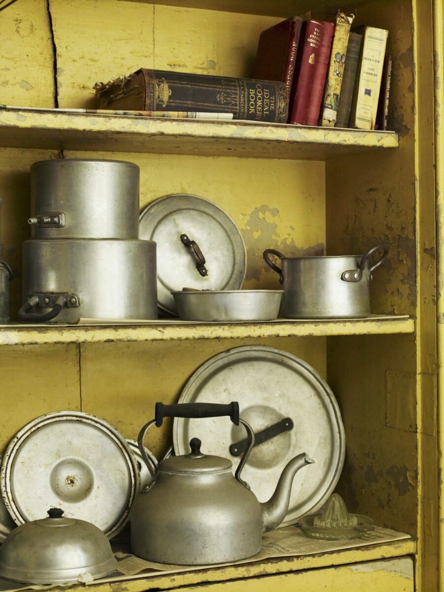 Old well worn recipe books and pots and pans on a kitchen shelf.